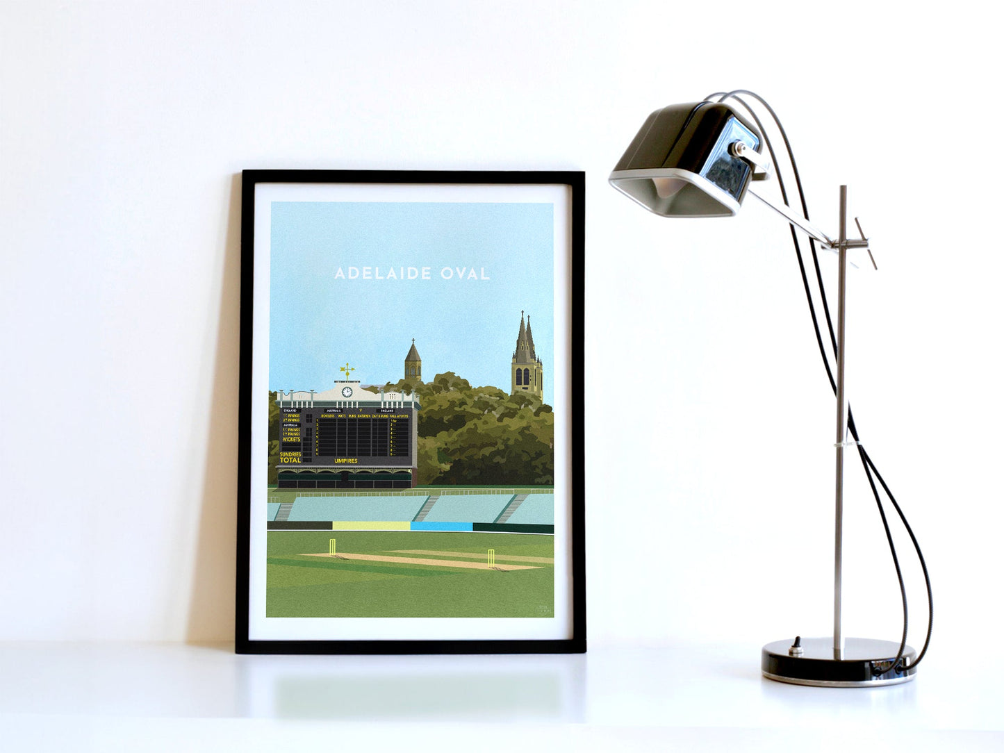 A contemporary style illustration of South Australia's cricket stadium, the Adelaide Oval, displayed as an art print within a black frame in a minimalist home office setting.