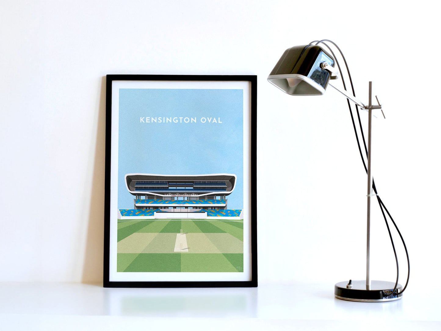 A contemporary style illustration of West Indies / Barbados cricket stadium, the Kensington Oval, displayed as an art print within a black frame in a minimalist home office setting.
