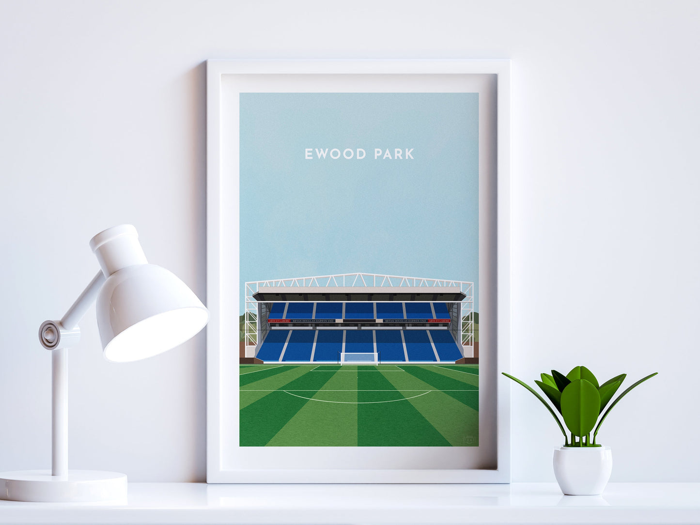 A contemporary style illustration of Blackburn Rovers' football stadium, Ewood Park, displayed as an art print within a white frame in a minimalist home office setting.