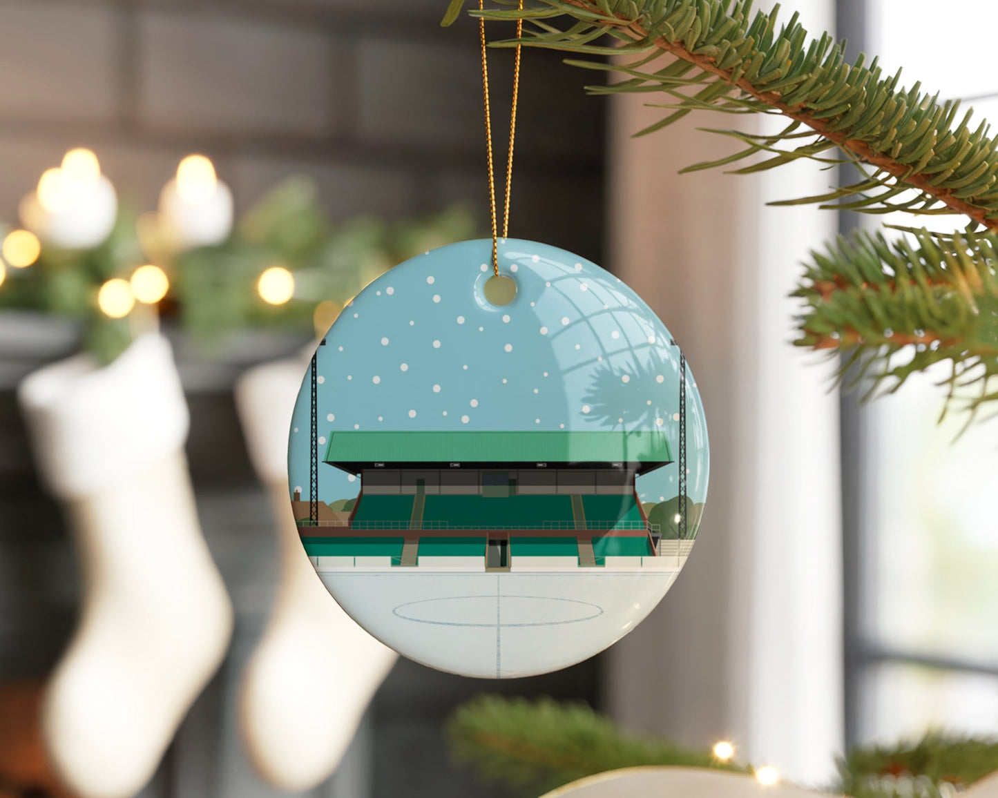 Ceramic Christmas bauble decoration hanging in a Xmas tree, featuring minimalist illustrations of Blyth Spartan's stadium, Croft Park, with snow falling in the sky and laid on the pitch.