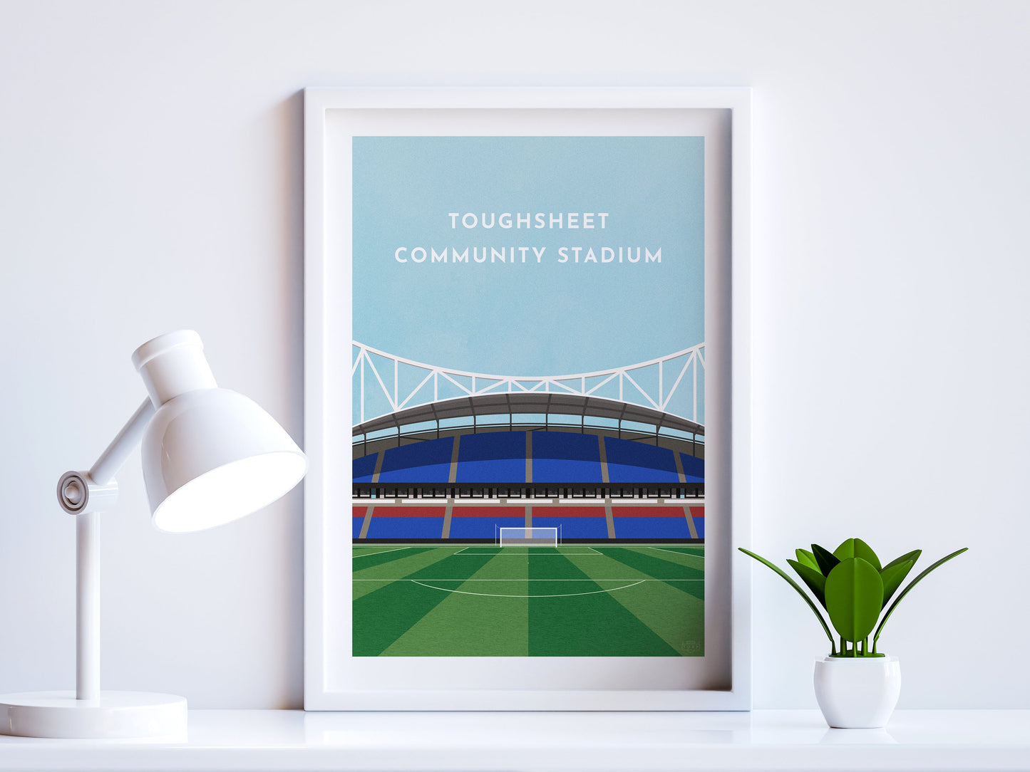 A contemporary style illustration of Bolton Wanderers' football stadium, the Toughsheet Community Stadium, displayed as an art print within a white frame in a minimalist home office setting.