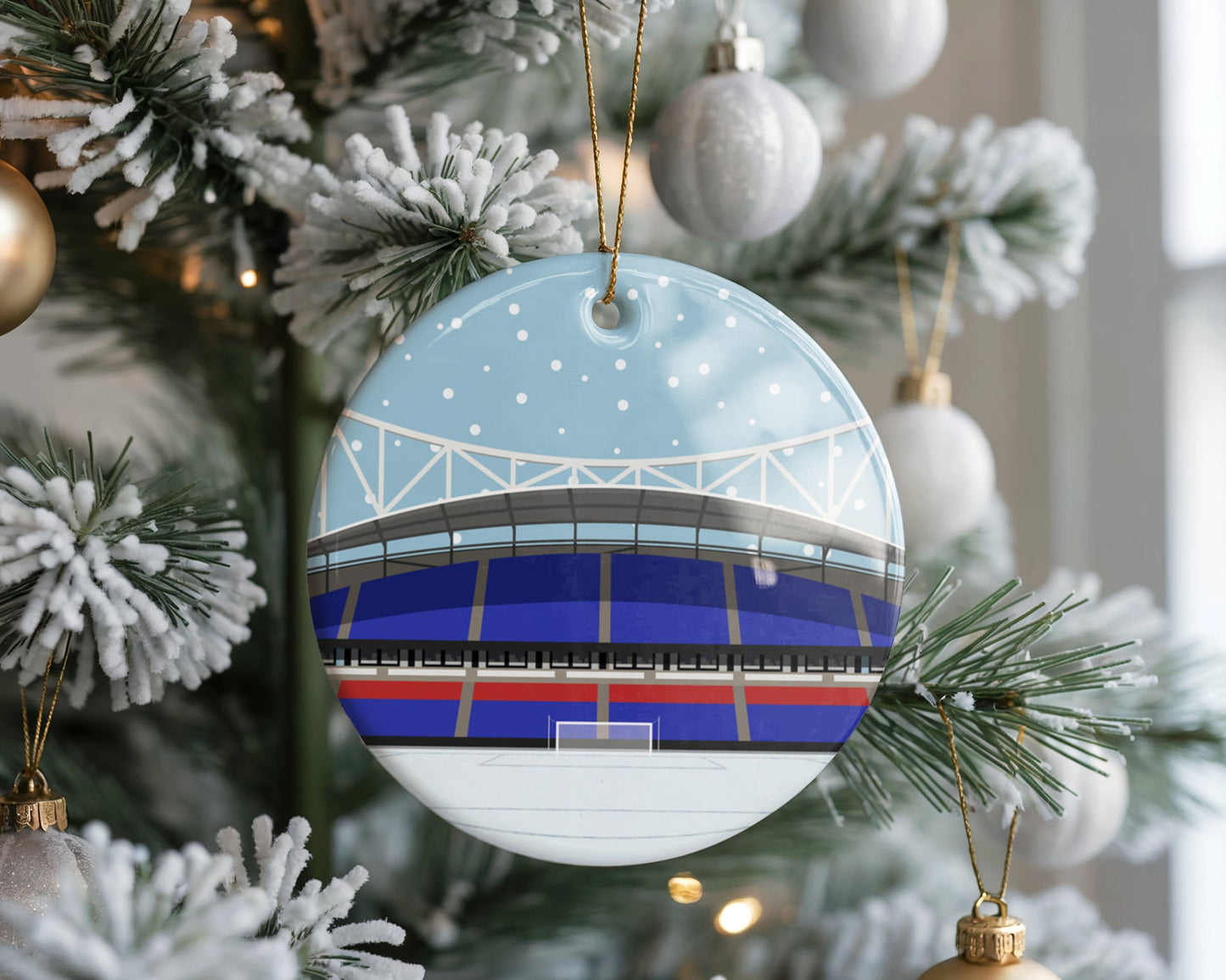 Ceramic Christmas bauble decoration hanging in a Xmas tree, featuring minimalist illustrations of Bolton Wanderer's stadium, the Toughsheet Community Stadium, with snow falling in the sky and laid on the pitch.