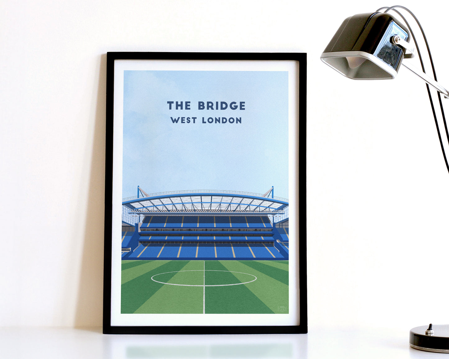 A modern style Chelsea Print, featuring a contemporary illustration of their home stadium the Stamford Bridge in West London, displayed within a black frame.