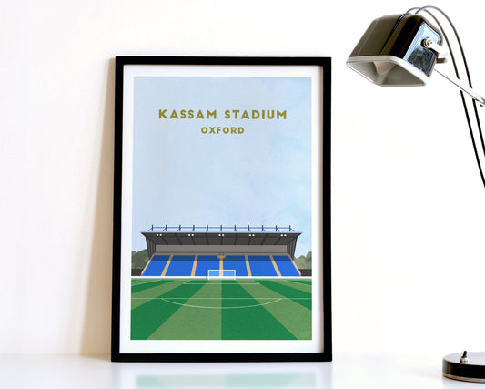 A modern style Oxford United Print, featuring a contemporary illustration of their home stadium the Kassam Stadium in Oxford, displayed within a black frame.