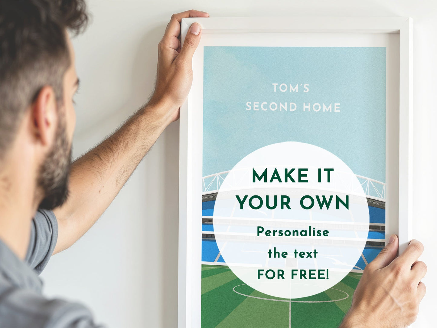 A photo of a man holding up a personalised white framed stadium print that he has received as a gift, that reads 'TOM'S SECOND HOME' as the text at the top. Text overlay reads: MAKE IT YOUR OWN Personalise FOR FREE!
