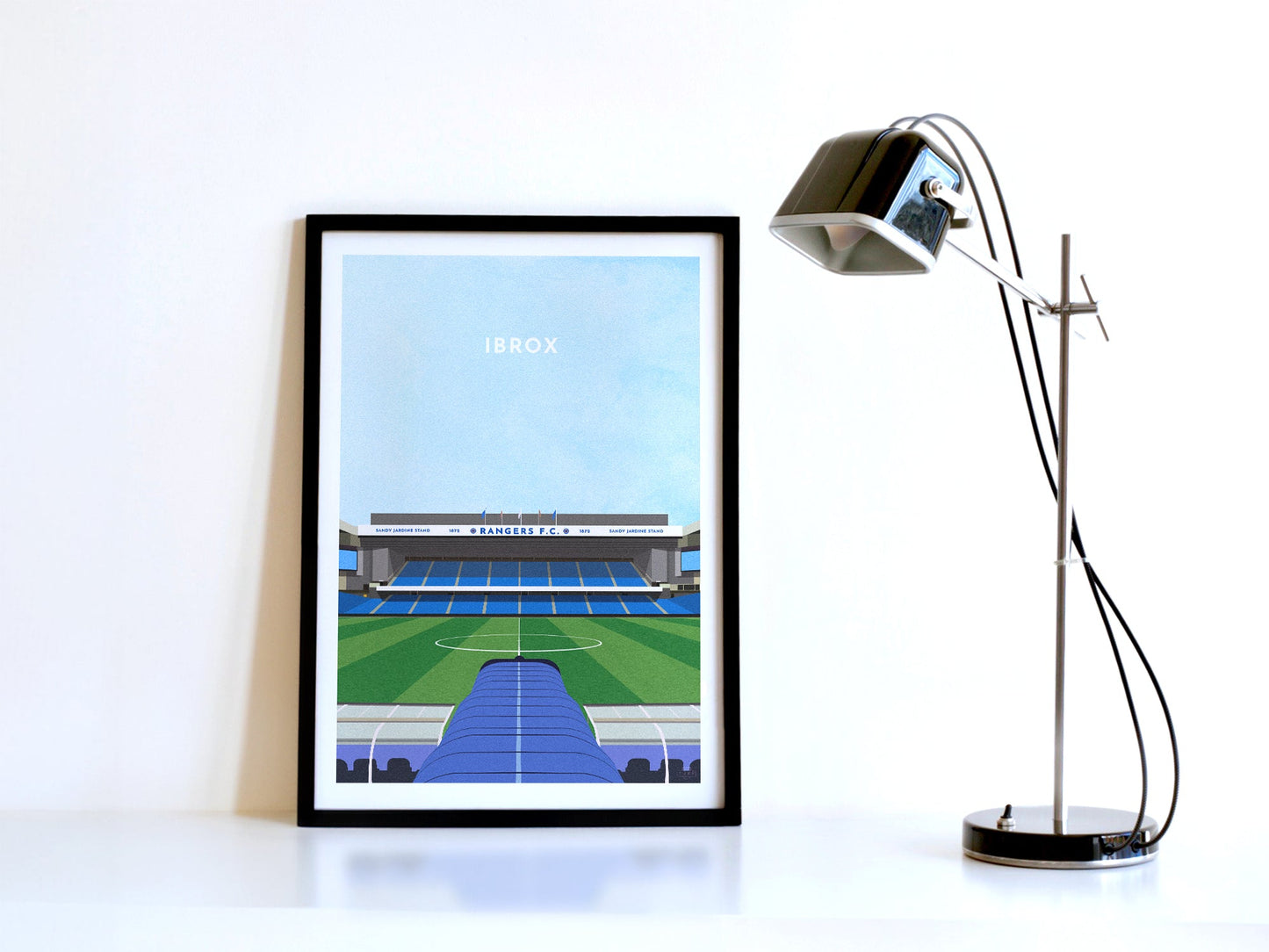 A contemporary style illustration of Rangers football stadium, Ibrox, displayed as an art print within a black frame in a minimalist home office setting.