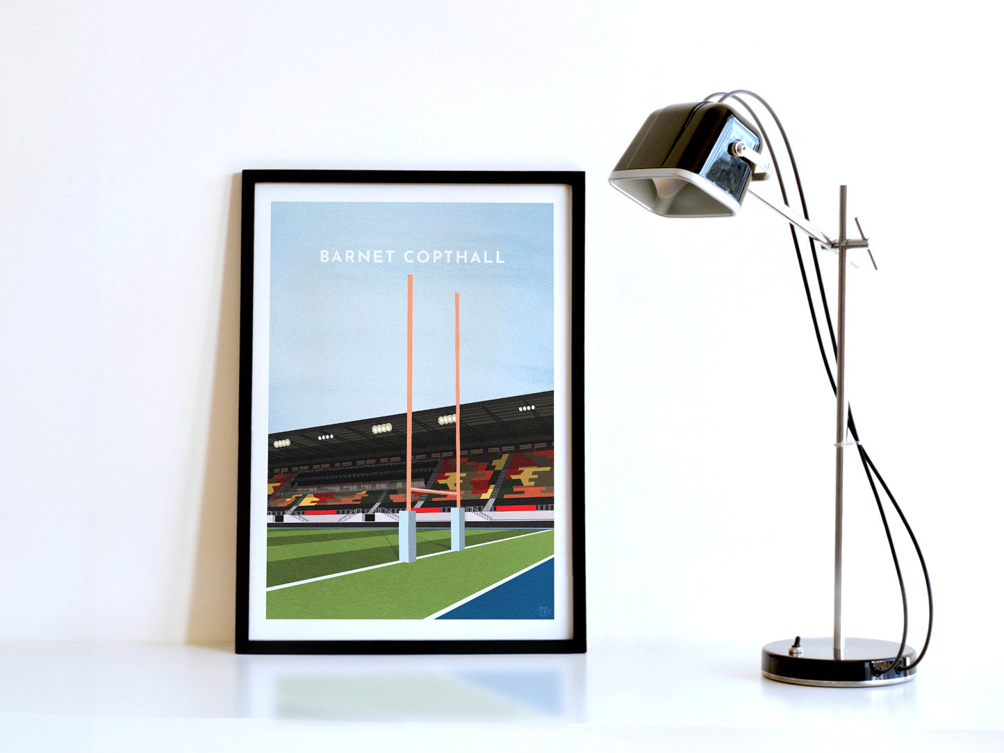 A contemporary style illustration of Saracens' Rugby stadium, the StoneX Stadium / Barnet Copthall, displayed as an art print within a black frame in a minimalist home office setting.