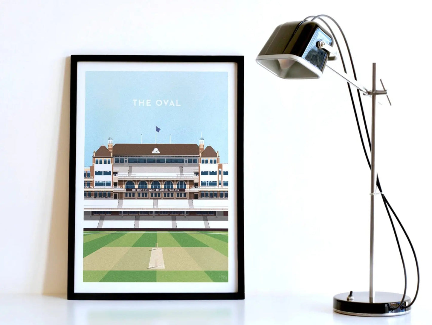 A contemporary style illustration of England and Surrey's cricket stadium, The Oval, displayed as an art print within a black frame in a minimalist home office setting.