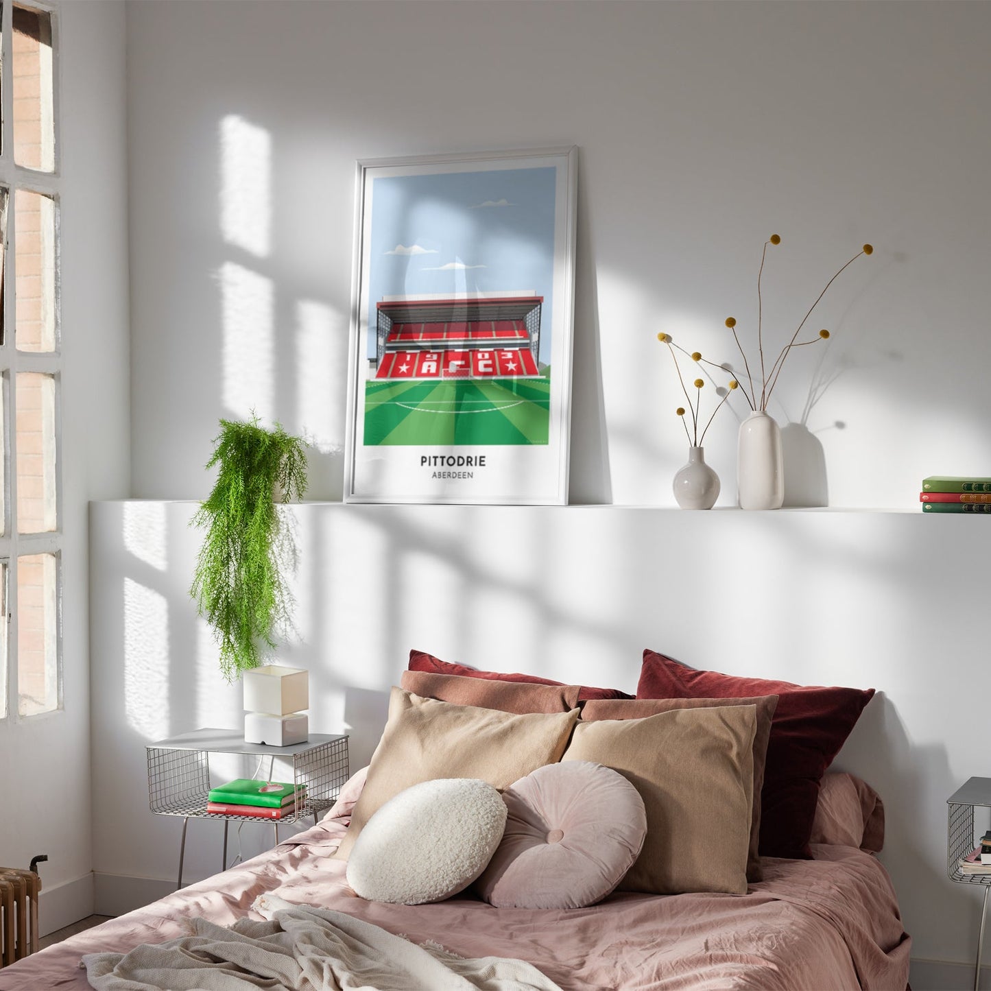 Framed illustrated print of Pittodrie in Aberdeen, home to Aberdeen, showcasing a minimalist design with vibrant red stands, green football pitch, under a blue sky.