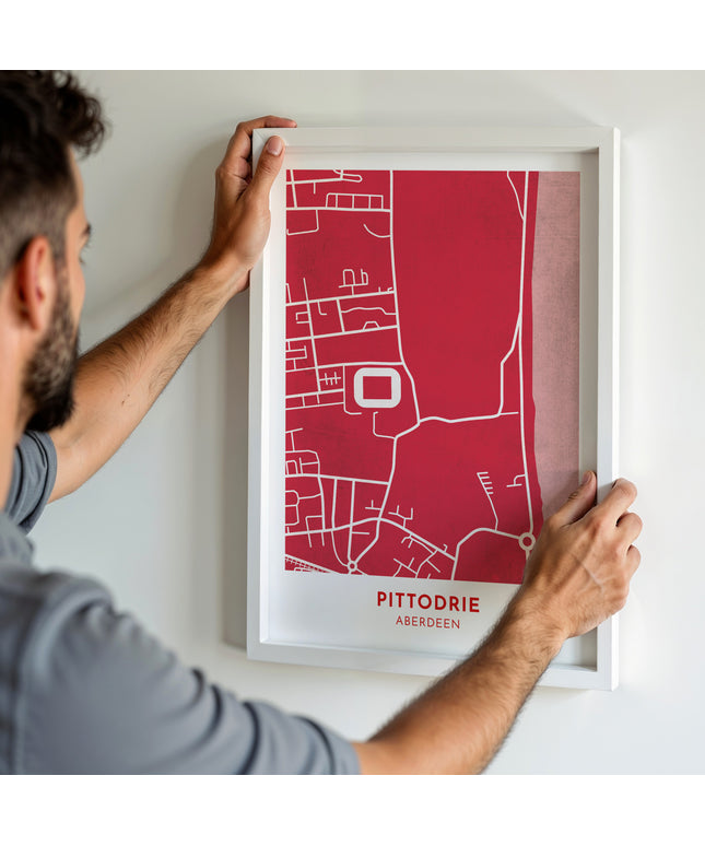 A man hanging a framed art print, featuring a contemporary style map illustration of Pittodrie, home to Aberdeen.