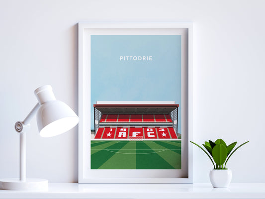 A contemporary style illustration of Aberdeen's football stadium, Pittodrie, displayed as an art print within a white frame in a minimalist home office setting.