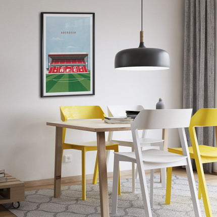 Framed illustration print of Pittodrie NAME in Aberdeen, home to Aberdeen, showcasing a minimalist design with vibrant red stands, green football pitch, under a blue sky.
