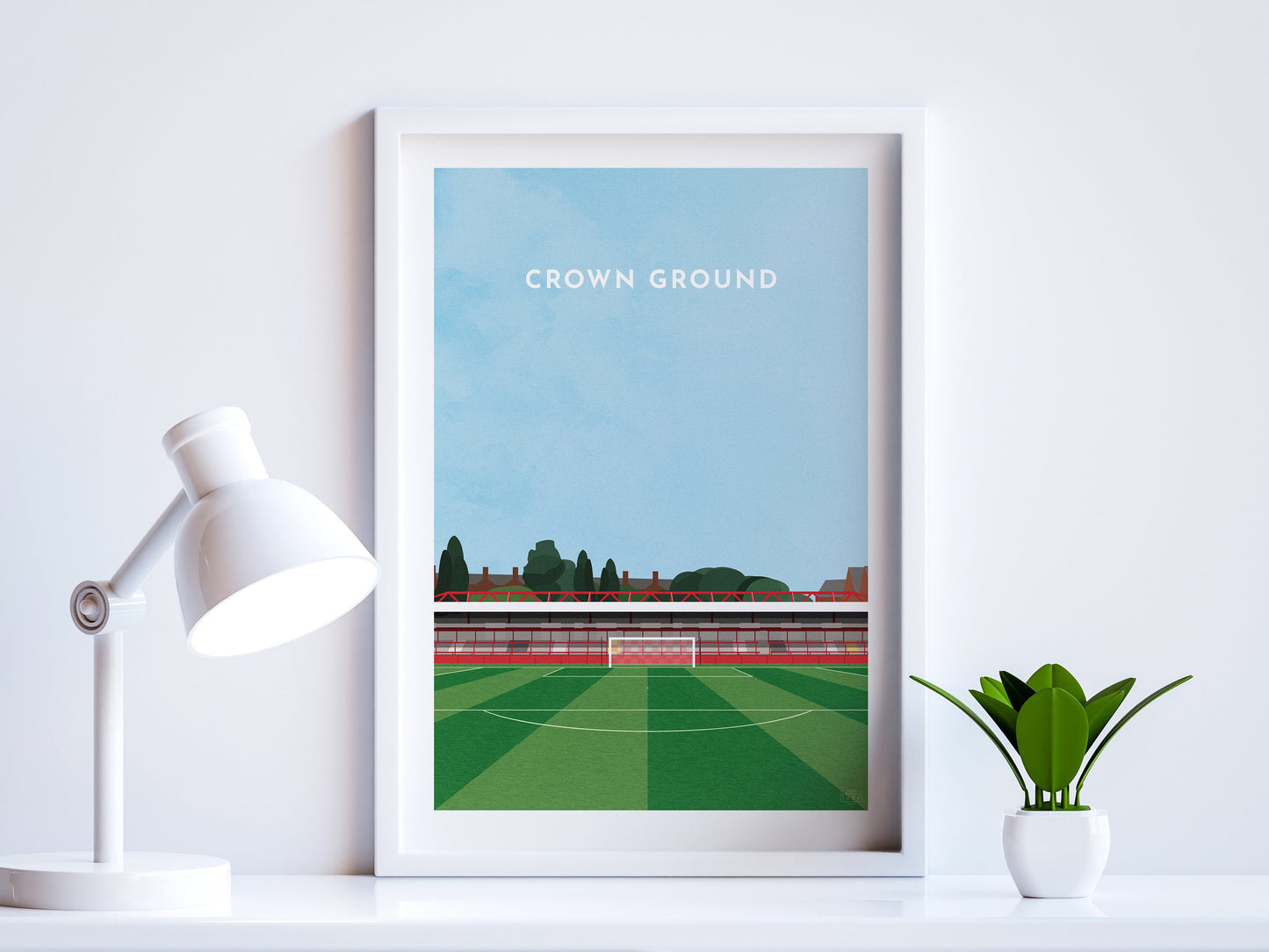 A contemporary style illustration of Accrington Stanley's football stadium, The Crown Ground / Wham Stadium, displayed as an art print within a white frame in a minimalist home office setting.