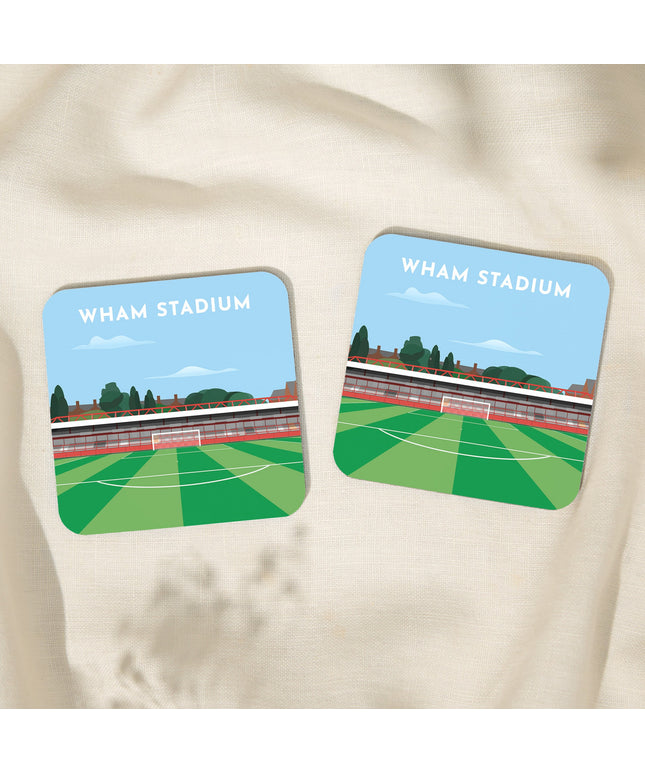 Two Square hardwood coasters laid on a tablecloth with glossy sublimation printed finish featuring contemporary illustration of Wham Stadium in Accrington, home to Accrington Stanley, showcasing a minimalist design with vibrant red stands, green football pitch, and the iconic stadium roof structure under a blue sky.