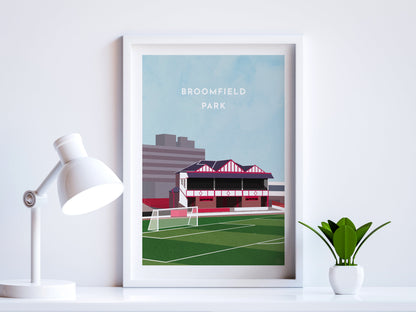 A contemporary style illustration of Airdrieonians' former football stadium, Broomfield Park, displayed as an art print within a white frame in a minimalist home office setting. 
