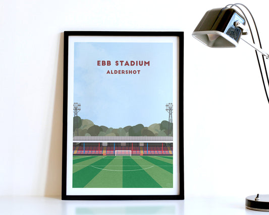 A modern style Aldershot Town Poster, featuring a contemporary illustration of their home stadium the EBB Stadium in Aldershot, displayed within a black frame.