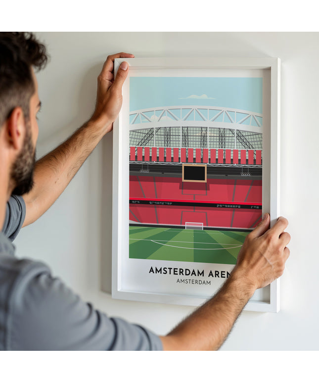 A man hanging a framed art print, featuring a contemporary style illustration of Amsterdam Area, home to Ajax and Netherlands.