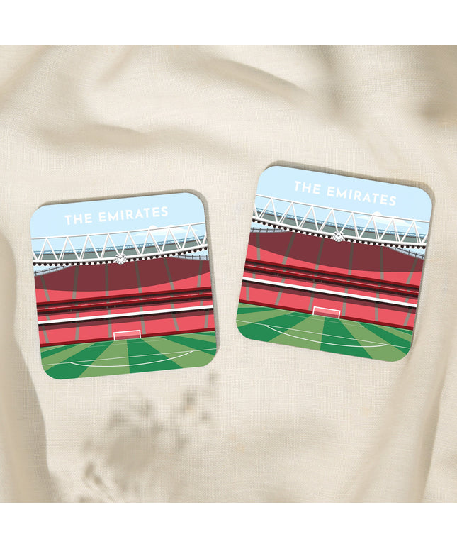 Two Square hardwood coasters laid on a tablecloth with glossy sublimation printed finish featuring contemporary illustration of The Emirates in North London, home to Arsenal, showcasing a minimalist design with vibrant red stands, green football pitch, under a blue sky.