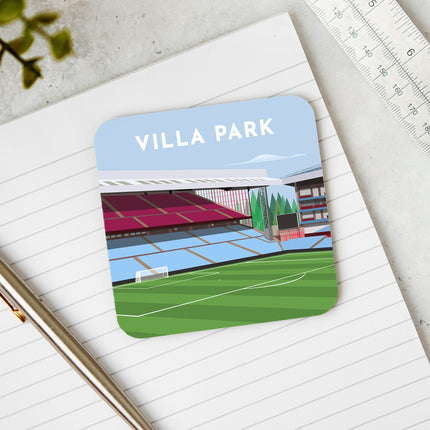 Square hardwood coaster placed on a desk, with glossy sublimation printed finish featuring contemporary illustration of Villa Park in Birmingham, home to Aston V, showcasing a minimalist design with vibrant claret & blue stands, green football pitch, under a blue sky.