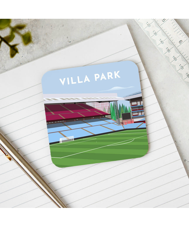 Square hardwood coaster placed on a desk, with glossy sublimation printed finish featuring contemporary illustration of Villa Park in Birmingham, home to Aston V, showcasing a minimalist design with vibrant claret & blue stands, green football pitch, under a blue sky.