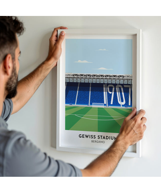 A man hanging a framed art print, featuring a contemporary style illustration of Gewiss Stadium, home to Atalanta.