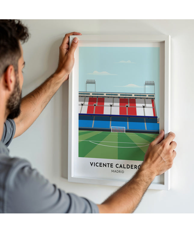 A man hanging a framed art print, featuring a contemporary style illustration of Vicente Calderon, home to Atlético Madrid.
