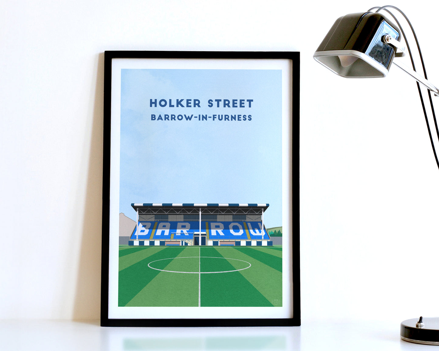 A modern style Barrow AFC Print, featuring a contemporary illustration of their home stadium the Holker Street in Barrow in Furness, displayed within a black frame.