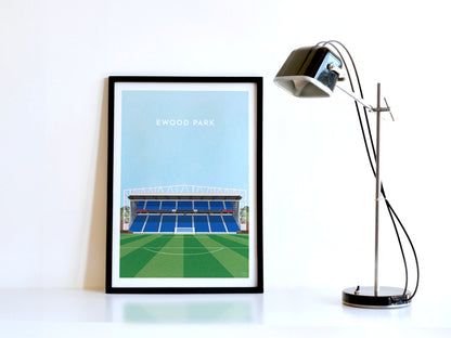 A contemporary style illustration of Blackburn Rovers' football stadium, Ewood Park, displayed as an art print within a black frame in a minimalist home office setting. 
