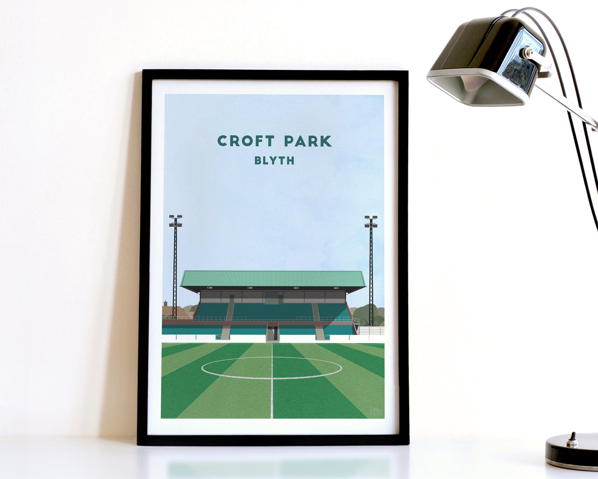 A modern style Blyth Spartans Print, featuring a contemporary illustration of their home stadium Croft Park in Blyth, displayed within a black frame.