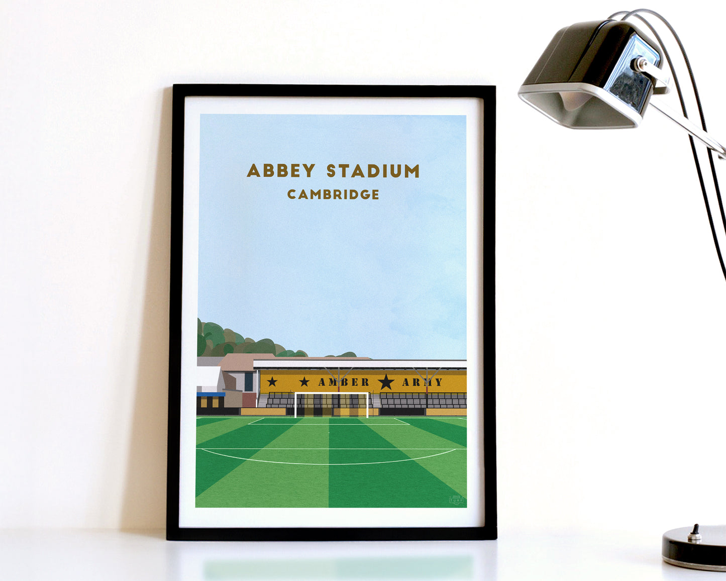 A modern style Cambridge United Print, featuring a contemporary illustration of their home stadium the Abbey Stadium in Cambridge, displayed within a black frame.