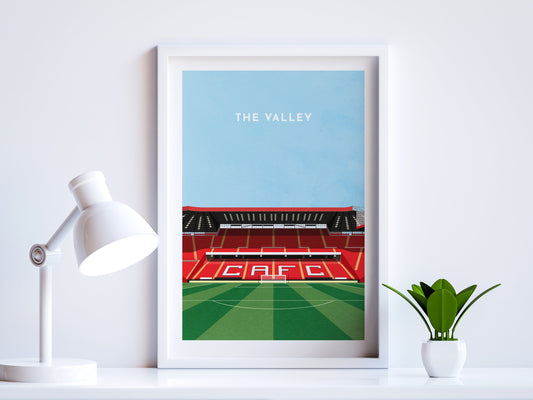 A contemporary style illustration of Charlton Athletic's football stadium, The Valley, displayed as an art print within a white frame in a minimalist home office setting. 