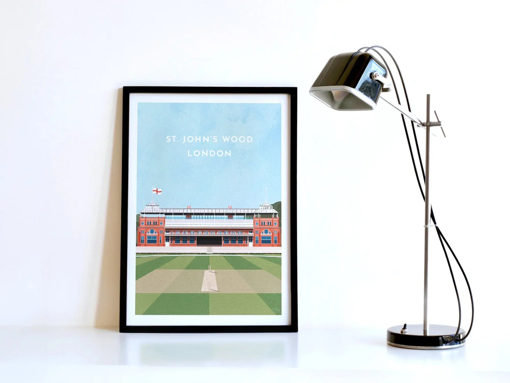 A contemporary style illustration of England cricket's ground, Lord's, displayed as an art print within a black frame in a minimalist home office setting. 
