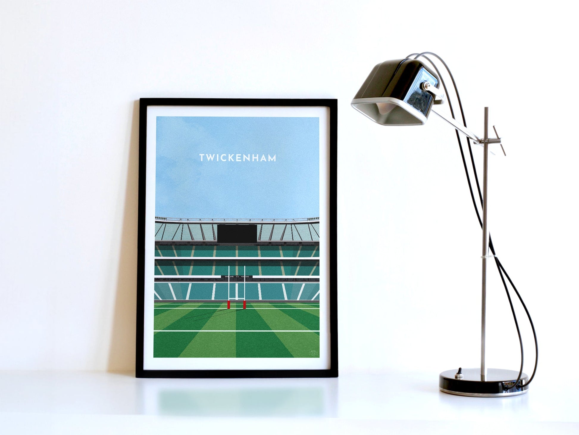 A contemporary style illustration of England's rugby stadium, Twickenham, displayed as an art print within a black frame, next to a retro style black lamp.