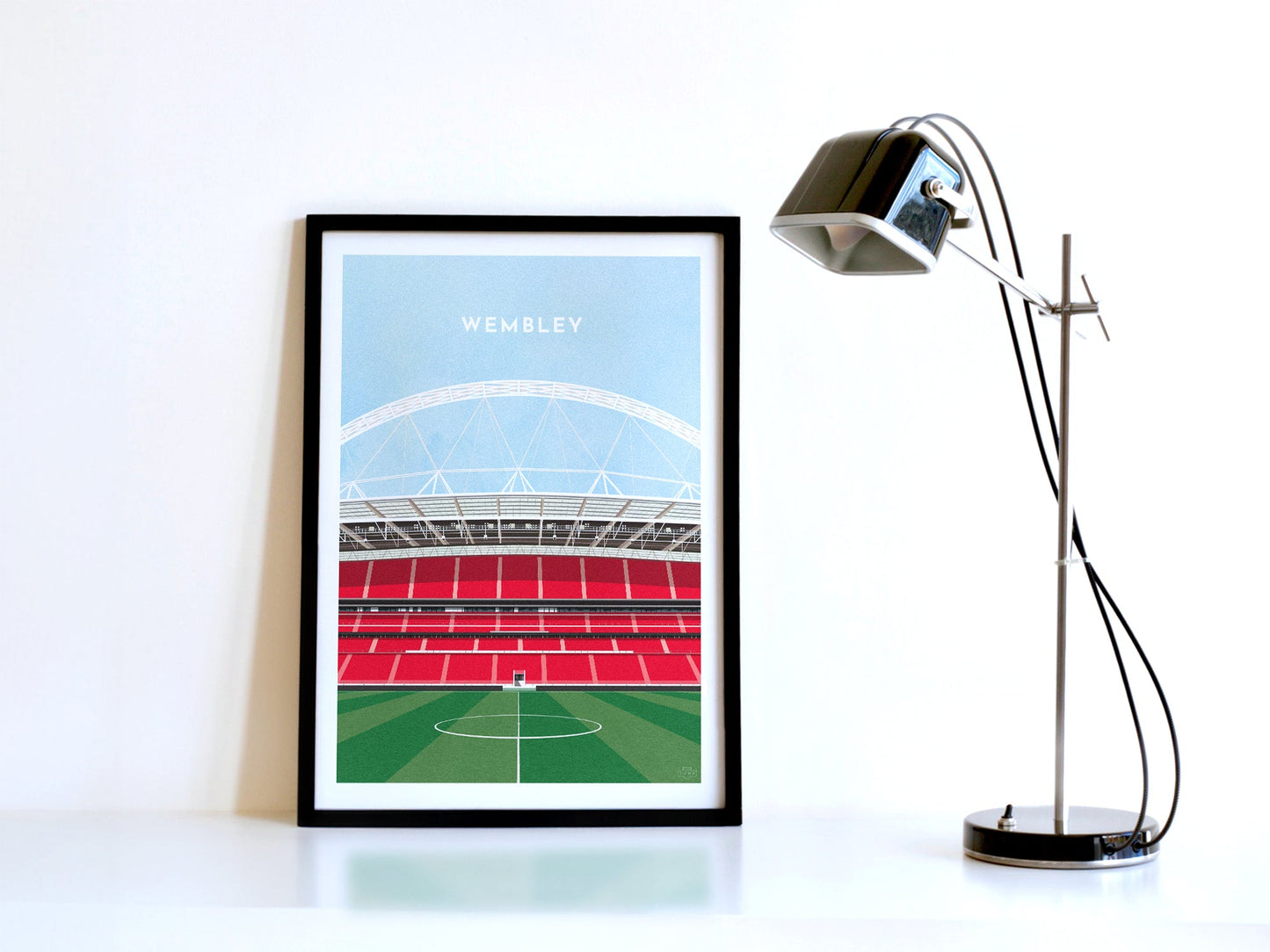 A contemporary style illustration of England's football stadium, Wembley, displayed as an art print within a black frame in a minimalist home office setting. 