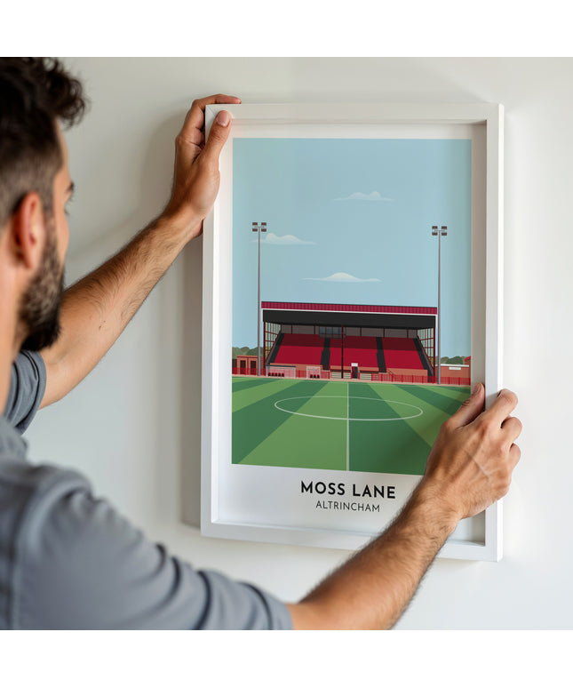 A man hanging a framed art print, featuring a contemporary style illustration of Moss Lane, home to Altrincham.