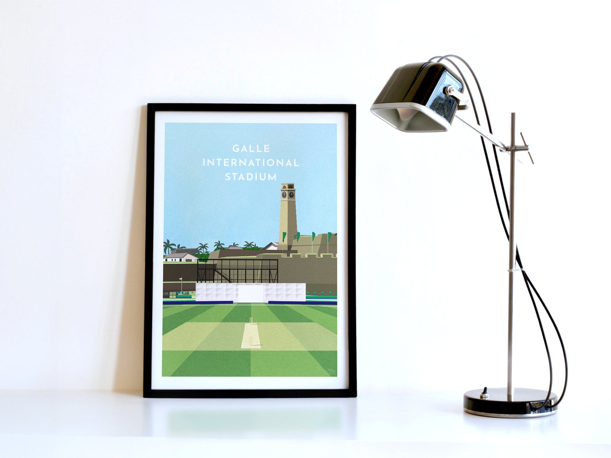 A contemporary style illustration of Sri Lanka's cricket stadium, Galle International Stadium, displayed as an art print within a black frame in a minimalist home office setting. 