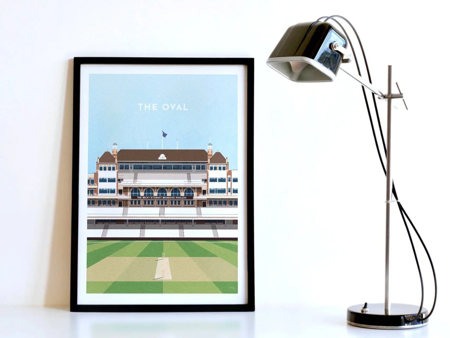 A contemporary style illustration of England and Surrey's cricket stadium, The Oval, displayed as an art print within a black frame in a minimalist home office setting. 