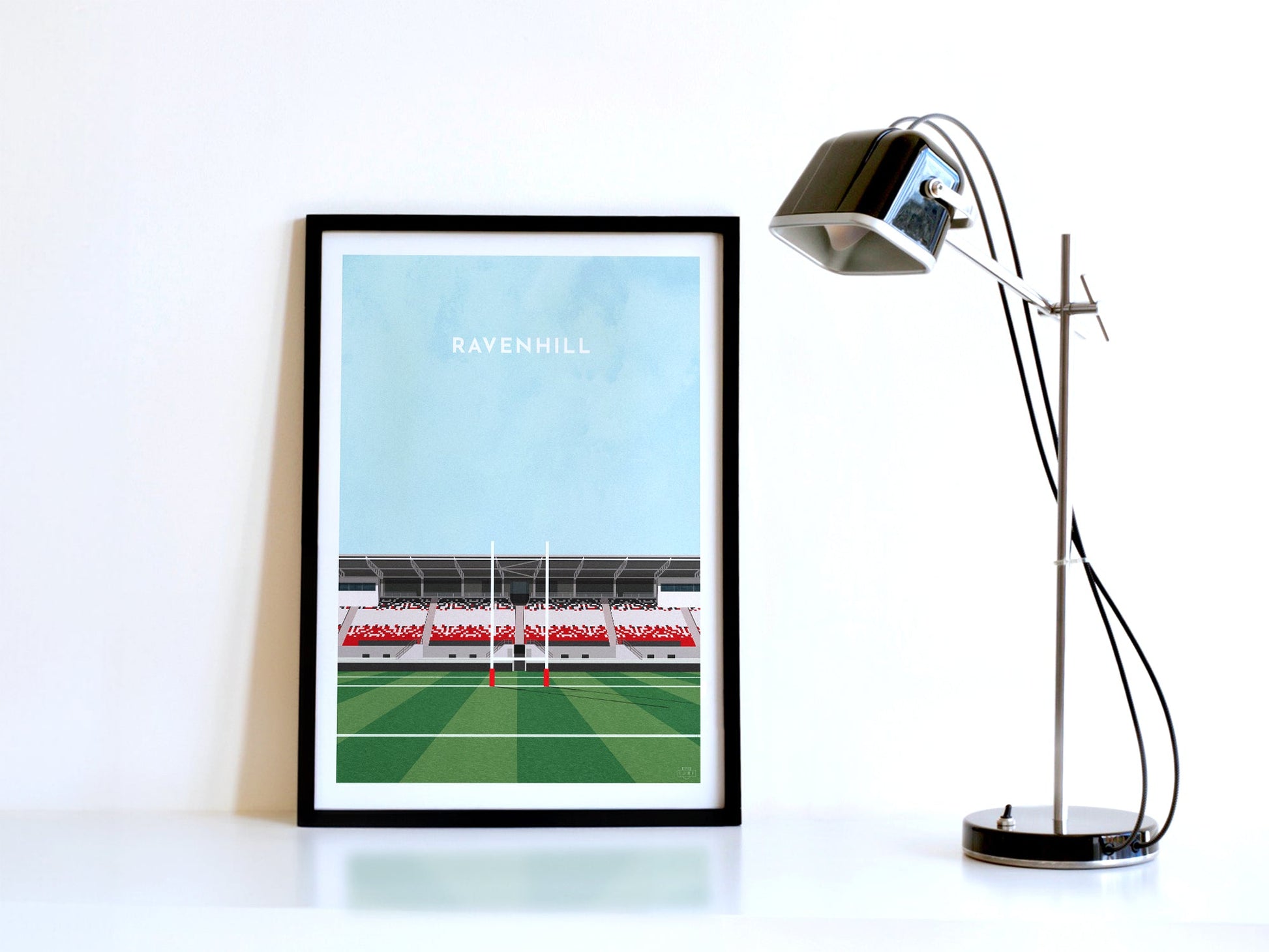 A contemporary style illustration of Ulster Rugby's rugby stadium, Ravenhill / Kingspan Stadium, displayed as an art print within a black frame in a minimalist home office setting. 