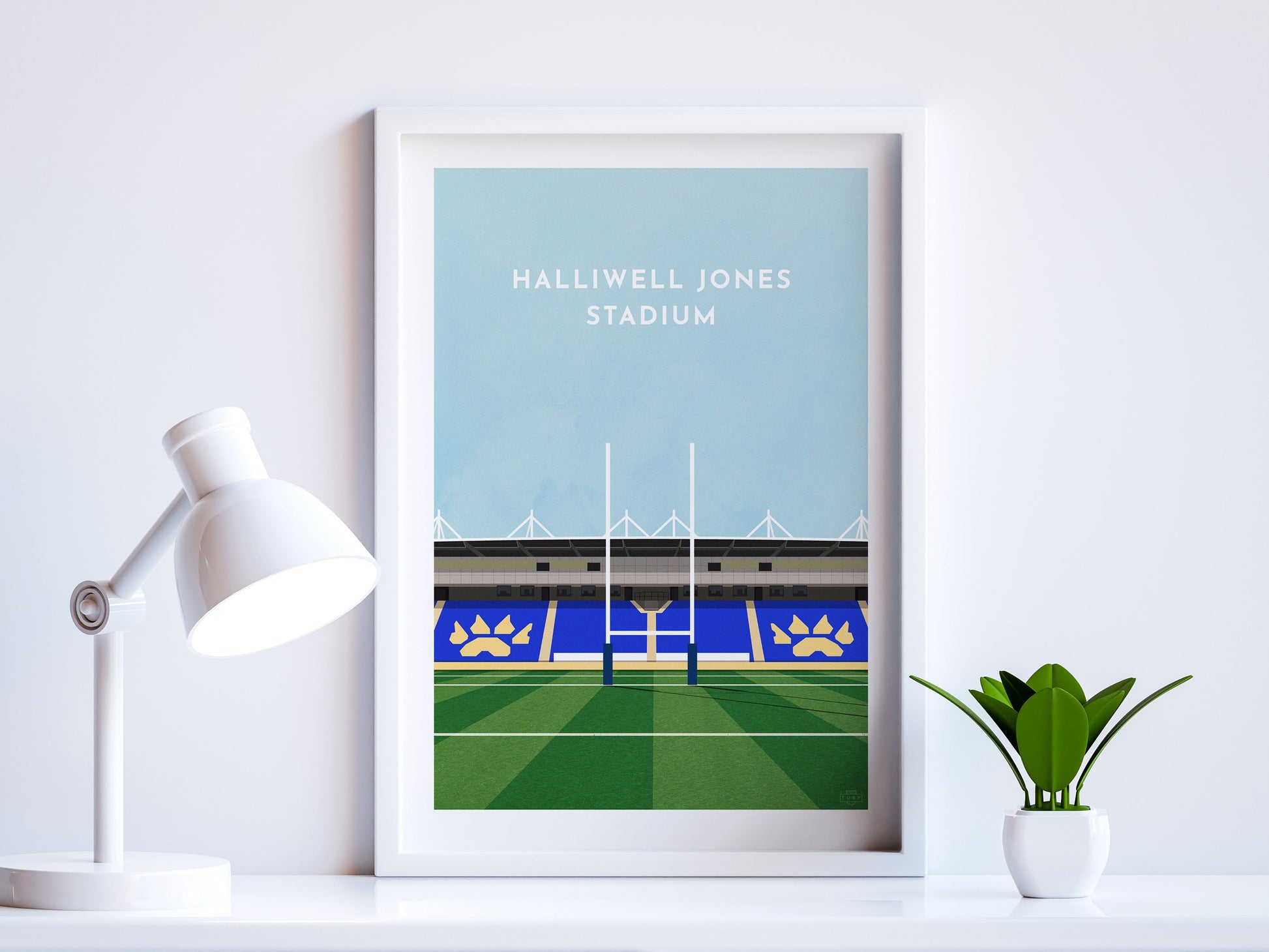 A contemporary style illustration of Warrington's Rugby stadium, the Halliwell Jones Stadium, displayed as an art print within a white frame in a minimalist home office setting. 