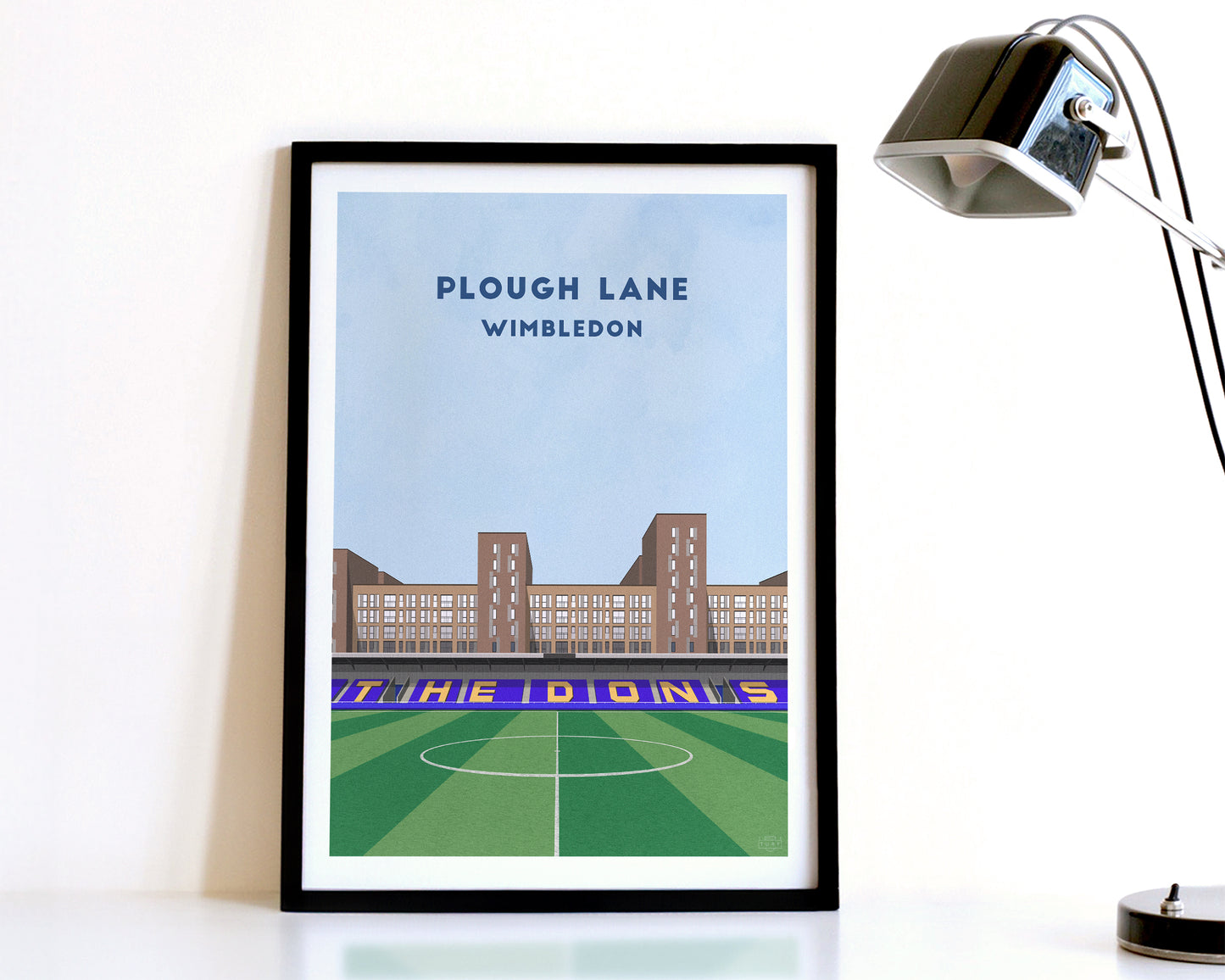 A modern style Wimbledon Print, featuring a contemporary illustration of their home stadium the Plough Lane in South London, displayed within a black frame.